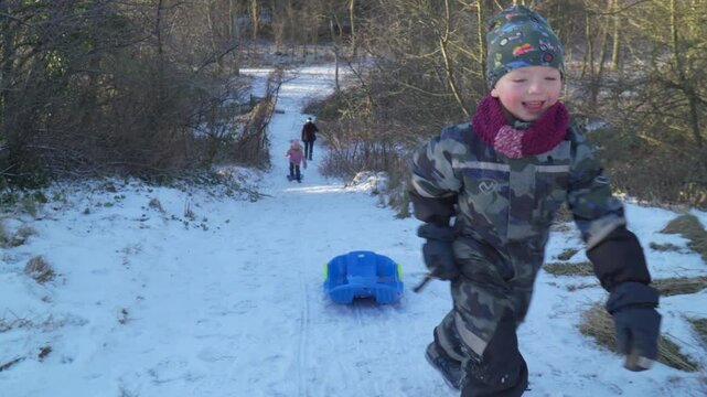 Boy walking up a snowy hill pulling a bobsled