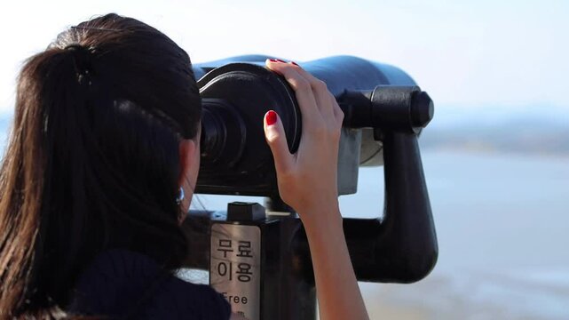 Korean girl back view face unrecognized looking into binoculars on North Korean at Korean Demilitarized Zone