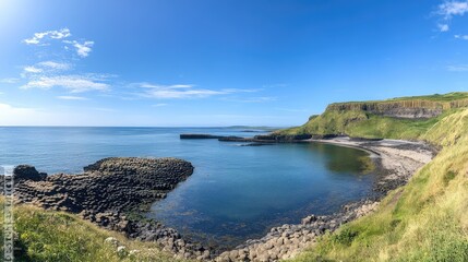Panoramic shot of the Giant's Causeway hexagonal rock formations stretching into the ocean, with green cliffs in the background. No people included.