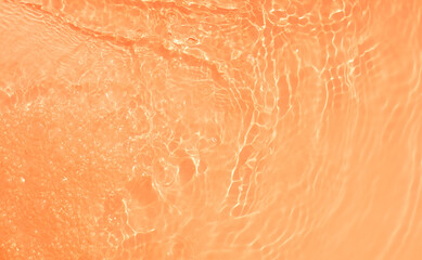 Orange water with ripples on the surface. Defocus blurred transparent blue colored clear calm water surface texture with splashes and bubbles. Water waves with shining pattern texture background.