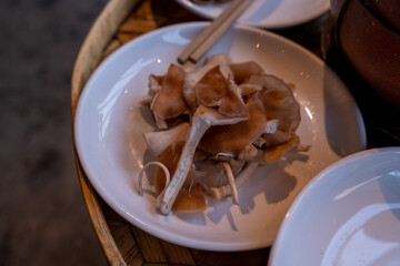 A close-up shot of various types of mushrooms and tofu slices arranged on white ceramic plates, placed around a traditional clay pot on a bamboo tray. 