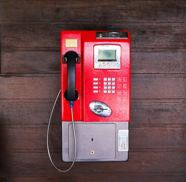 Public red old payphone coin clinging with brown wooden wall in Thailand. It is not popular now. Since most people use cell phones. But still found in the countryside. For vintage interior decoration.