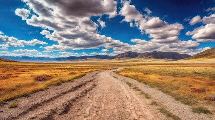 Fototapeta premium The Dusty Dirt Track Road. Highway in to the mountains, with blue skies and clouds. Ideal Desktop background or Wallpaper.