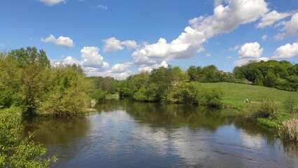 A peaceful river flowing through lush greenery under a bright blue sky with fluffy clouds during a sunny day