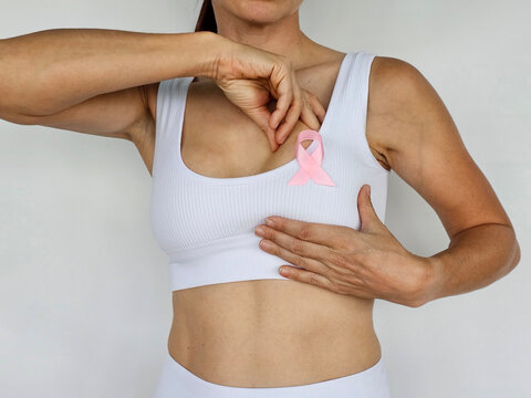 Woman with pink ribbon on her chest to promote breast cancer awareness. Woman palpating her breasts with her hands to prevent cancer