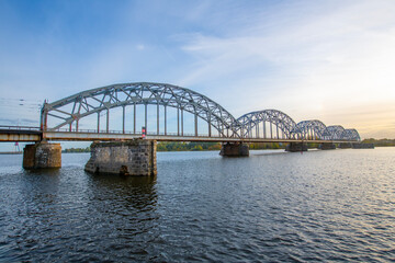 Obraz premium A modern electric passenger train crosses the railway bridge (Dzelzcea tilts) over the Daugava River. Taking passengers to the scenic Jurmala region of Latvia.