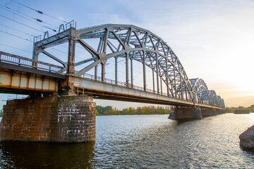 Fototapeta premium A modern electric passenger train crosses the railway bridge (Dzelzcea tilts) over the Daugava River. Taking passengers to the scenic Jurmala region of Latvia.