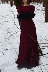 A red-haired girl in a burgundy dress with red lips. A woman with her arms crossed. Medieval style, Gothic atmosphere. The witch, the queen.