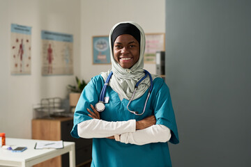 Muslim nurse smiling warmly in medical office with stethoscope around neck, showcasing professional attire and compassionate demeanor