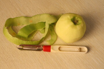 A Freshly Peeled Apple with a Peeler and Its Skin Displayed on a Wooden Table Surface