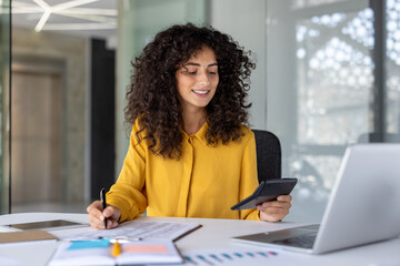 Latin American businesswoman accountant at office desk with calculator, pen, and laptop,...
