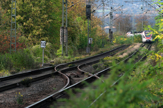 Zweigleisige Bahnstrecke mit B&auml;umen und Hecken im Herbst und Nahverkehrszug der Bahn im Hintergrund - Stockfoto