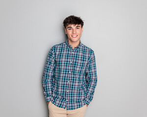 sexy young man in checkered shirt smiling while holding hands in pockets