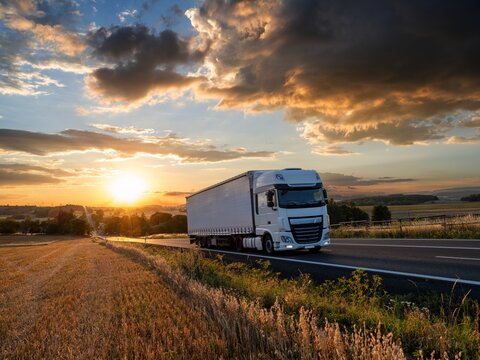 White truck driving on the asphalt road in rural landscape at a dramatic sunset