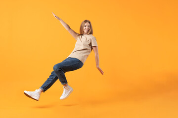 Lifestyle, business, commercial concept. A young woman mid-jump with a happy expression on an orange background