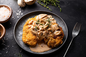 Fried chicken breast fillet in creamy mushroom sauce with champignons and oregano on the dark table