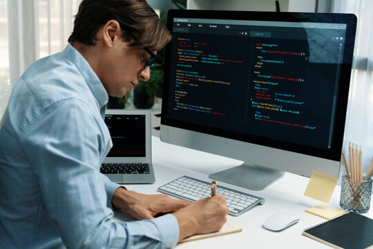 Stressful IT developer analyzing online software development information on pc and laptop with coding program on trial application project. Technical engineer writing crucial memo lists. Pecuniary.