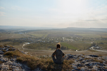 Fototapeta premium Person sitting on hill overlooking valley and town below on travel adventure trip discovery beauty nature landscape viewoptionsmenu