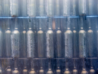 Rows of empty dark glass wine bottles in dirty transparent PVC stretch film front view