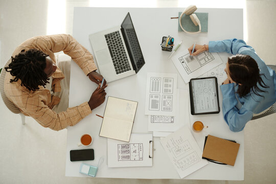 Two professionals engage in design project, sharing ideas and using various digital devices. Overhead view highlights tools and workspace arrangement
