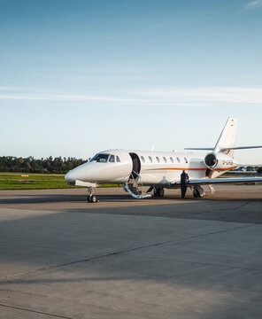 Front three quarter view of business jet on airport apron in the morning. Low morning sun casts long shadows on concrete surface. Friedrichshafen, Germany - September 19 2019.