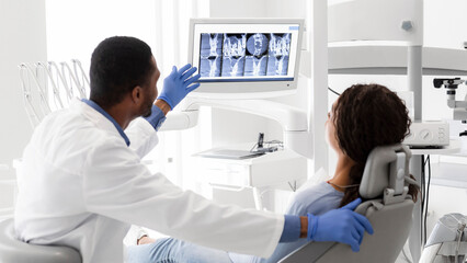 Obraz premium Black Dentist Explaining Xray On Screen To Female Patient At Clinic