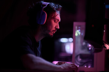 A devoted gamer sits in a vibrant neon lit room, completely engrossed in intense gameplay
