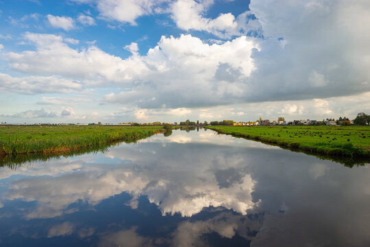 Beautiful view of a wide ditch in the vast meadows of the Voorofsche polder between Boskoop and Waddinxveen, Netherlands. The clouds are beautifully reflected in the calm water of the ditch.