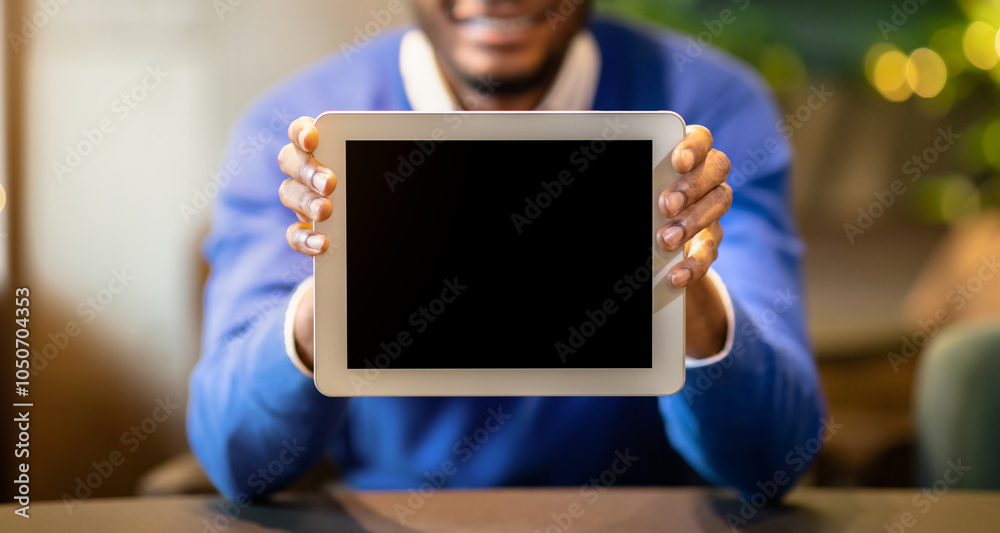 Poster cool app. black young man showing tablet computer blank screen sitting at loft cafe, mock up