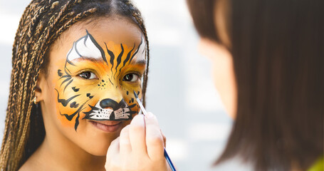 Adorable african-american girl getting tiger face painting in park, empty space