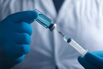 A blue-gloved medic's hand holds a syringe and test vaccine