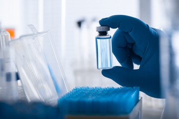 A scientist's hand in a medical glove holds a test tube with a substance