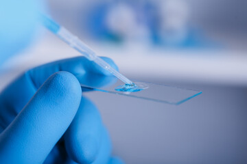 A scientist's hand in a glove holds a pipette and Microscope glass