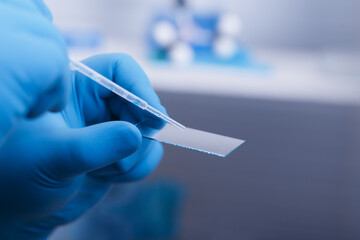 A scientist's hand in a glove holds a pipette and Microscope glass