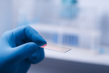 A scientist's hand in a glove holds a pipette and Microscope glass