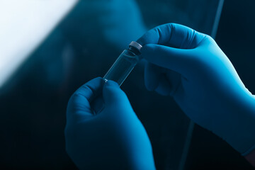 A blue-gloved medic's hand holds a vaccine or test tube