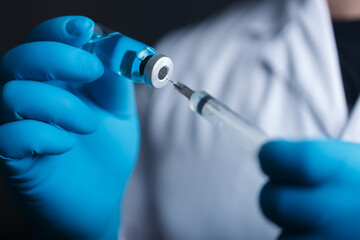 A blue-gloved medic's hand holds a syringe and test vaccine