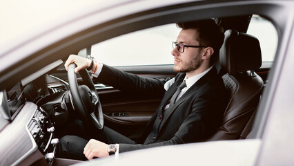 Confident Businessman Concept. Young man in glasses driving in luxury car, side view