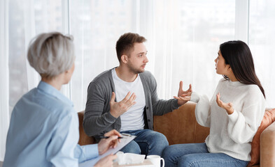 Fototapeta premium Family Conflicts. Married Couple Having Quarrel Blaming Each Other For Unhappy Life Sitting During Psychologist's Appointment In Office. Selective Focus