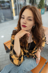 Beautiful fashionable young woman model in trendy clothes with shirt sitting on the street