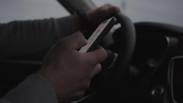 A man is driving a car and looking at his cell phone. Scene is somewhat tense, as the man is distracted by his phone while driving. This could be dangerous