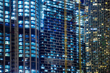 Bright lights illuminate the exteriors of towering skyscrapers in a vibrant city, showcasing construction activity against a nighttime backdrop. Night view of modern skyscrapers under construction.