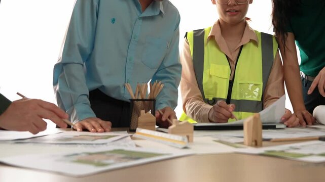 Smart architect and safety engineer discussion about building blueprint on table with architectural document, measurement tools and wooden block scatter around at modern office. Closeup. Delineation.