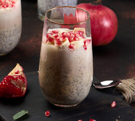 A glass of chia seeds and yogurt, with banana pieces and pomegranate seeds added to the dessert