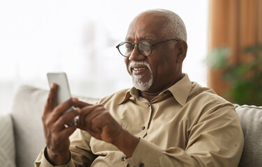 Senior Black Man Texting On Smartphone And Using Mobile Application Wearing Eyeglasses Sitting On...