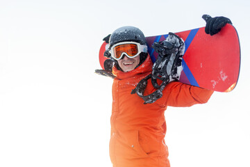 young cheerful guy in ski clothes holds snowboard and smiles at the resort, man in orange jacket,...