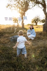 mother blowing soap bubbles while playing with her child in the garden at sunset