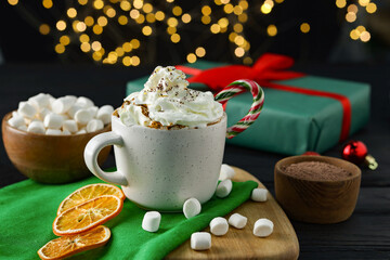 Tasty hot cocoa drink with whipped cream in cup and marshmallows on black wooden table, closeup