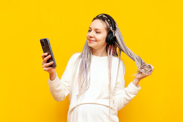 young girl with colored dreadlocks listening to music on headphones and using a smartphone on a...