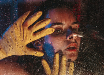 girl in cleaning gloves is behind wet glass